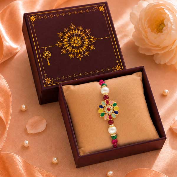 Open burgundy gift box with gold floral pattern, revealing a beaded bracelet with a multicolored flower pendant and pearl beads on a beige cushion.
