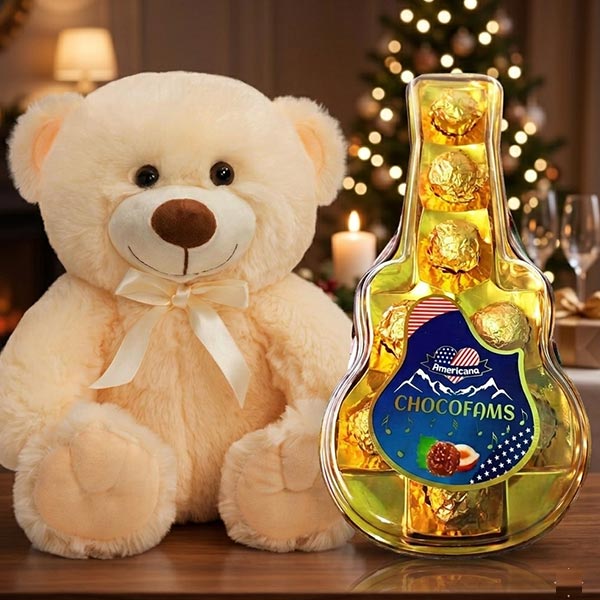 Cream-colored teddy bear with a white ribbon sits beside a guitar-shaped box of chocolates on a festive table.